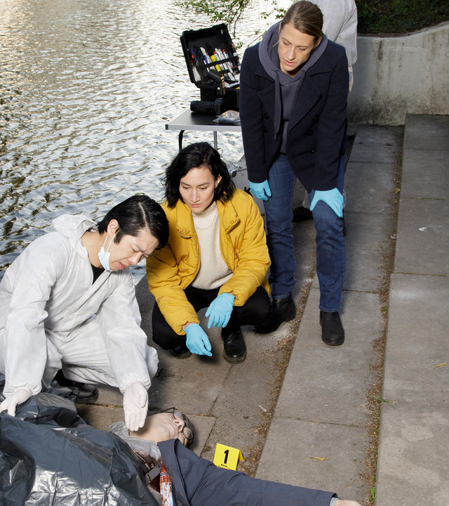 "SOKO Potsdam - Unter Kontrolle": Tamara Meurer (Anja Pahl) und Pauline Hobrecht (Agnes Decker) sind am Tatort beim Fluss an einer Treppe. Thomas Brandner (Yung Ngo) hockt neben ihnen vor der Leiche von Vadim Pasetzki (Komparse), an dessen Brust viel Blut zu sehen ist.