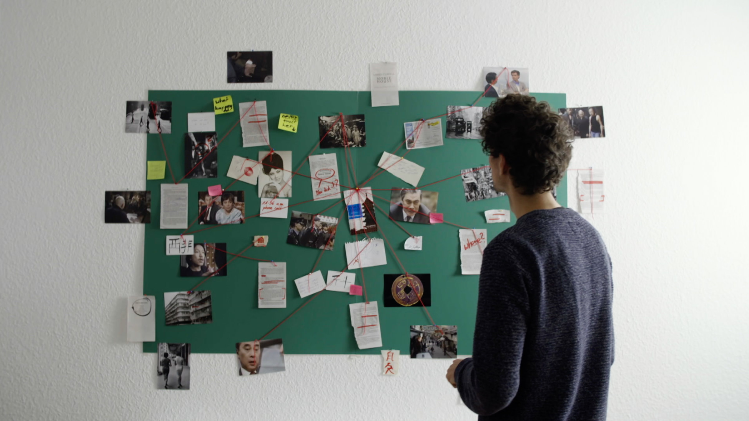 "Angstlust – Faszination True Crime": Ein Mann ist von hinten zu sehen. Er blickt auf eine Tafel, an der zahlreiche Fotos, Dokumente und Post-its angebracht sind, die durch eine rote Schnur miteinander verbunden sind.