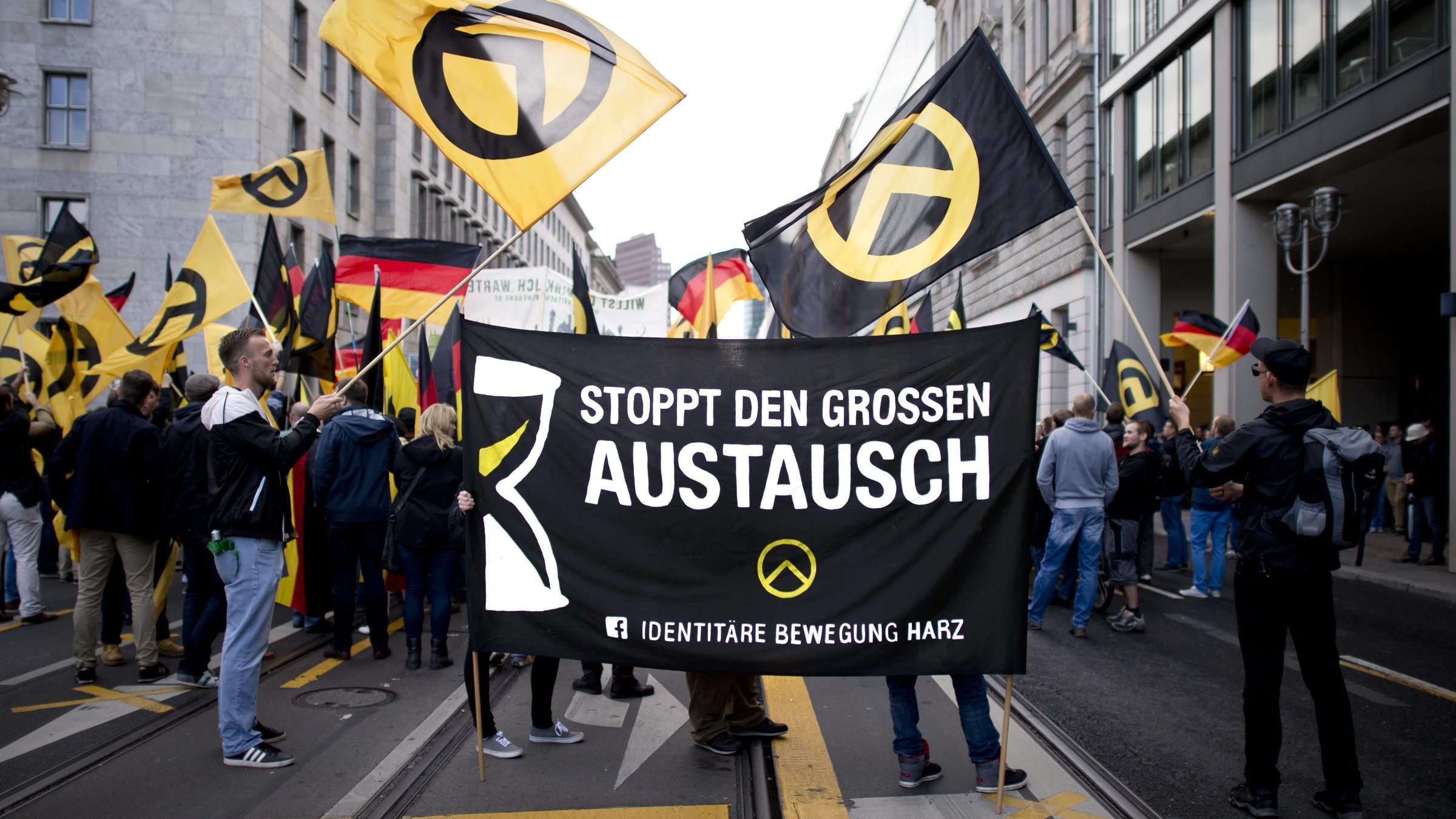 "Die Neue Rechte - Der Wahn vom homogenen Volk": Demonstration; Junge Männer schwenken Fahnen und halten Banner mit Aufschrift "Stoppt den großen Austausch" in die Kamera.