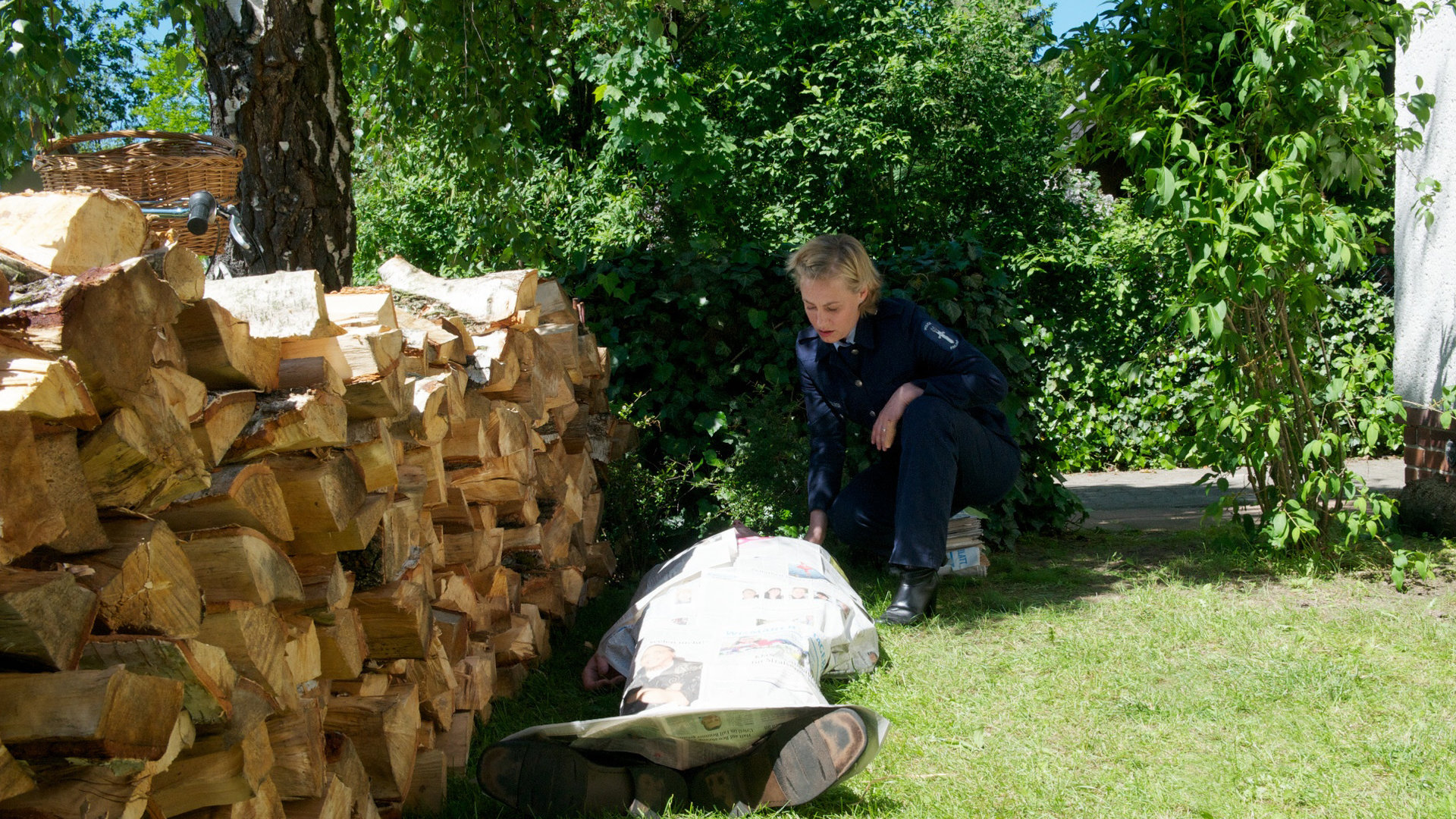"SOKO Wismar - Bankgeheimnis": Neben einer Brennholzreihe in einem Garten kniet Leena Virtanen (Li Hagman) neben einer zugedeckten Leiche.