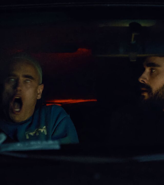 "Moresnet - The Book of Death: Ich bin nicht ich": Daan Schotz (Arend Pinoy) sitzt nachts auf dem Beifahrersitz eines Autos. Sein Mund ist aufgerissen, die Augen schauen nach oben unter die Augenlider - er hat einen Anfall. Sein Bruder Ben Schotz (Boris Van Severen) blickt sorgenvoll vom Fahrersitz zu ihm herüber.