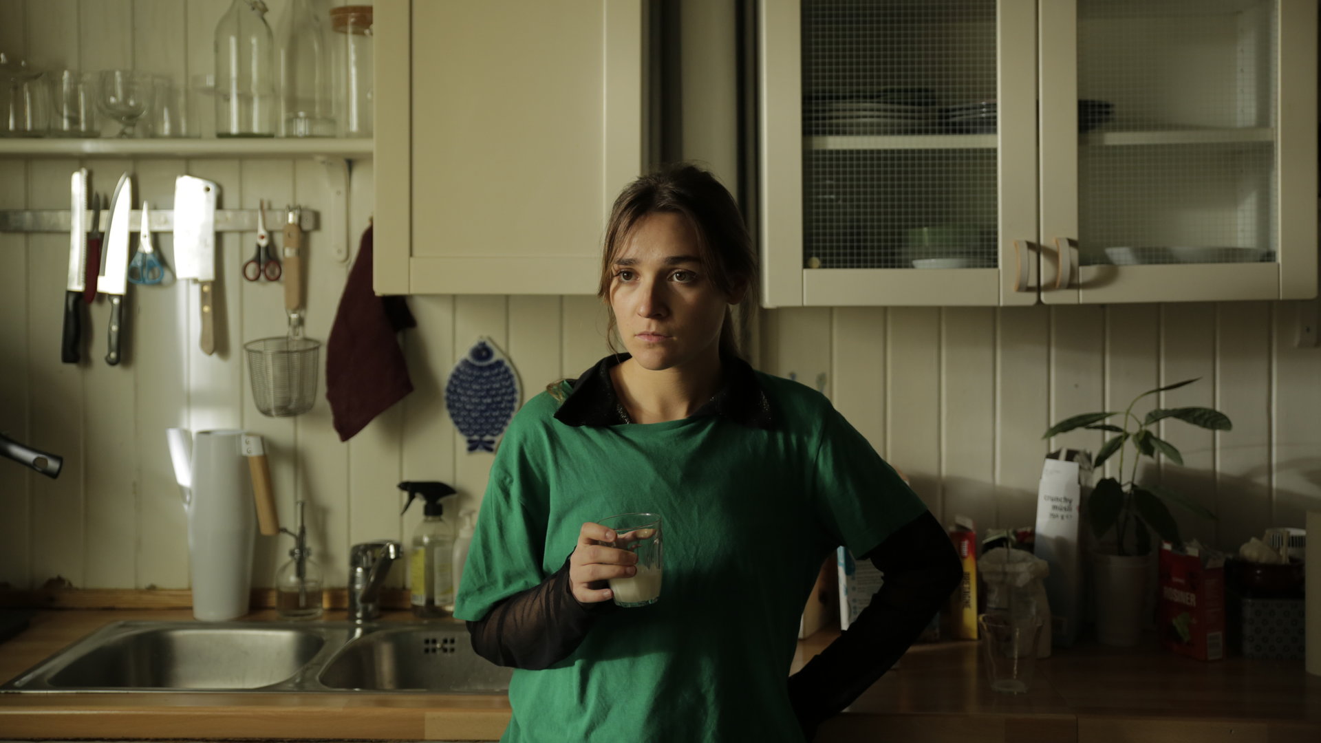 "About Saturday - Forever Singles": Klara (Darin Hagi) steht in einer Küche und schaut konzentriert in die Ferne, während sie ein Glas Milch in der Hand hält.