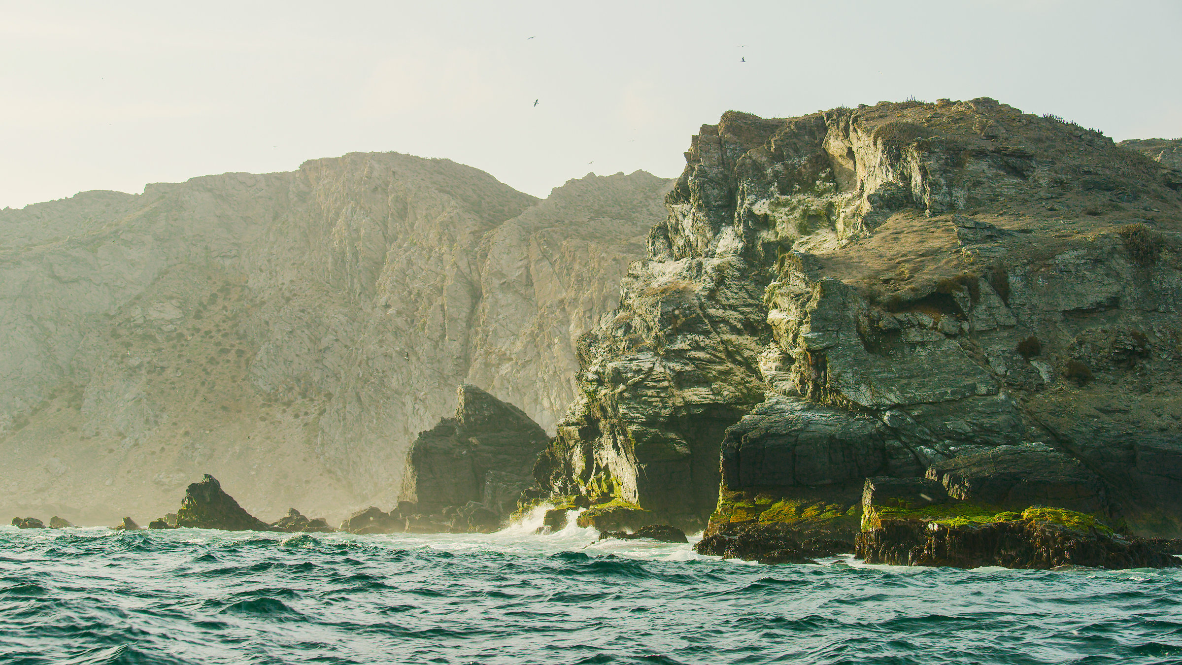 "Der Humboldt-Strom (2/3) - Die Küste der Atacama":  Leicht bewegte See trifft auf sonnenbeschienene Felsenküste.