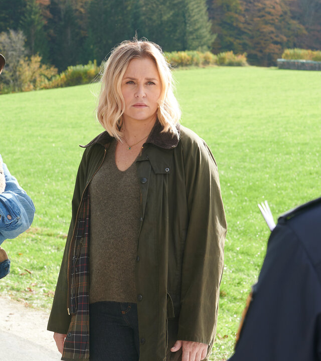 "Lena Lorenz - Gegen den Schmerz": Auf einer Straße stehen Schorschi Striebel (Sebastian Edtbauer) und Lena Lorenz (Judith Hoersch) und reden mit der Polizeibeamtin Anna Prückl (Sarah-Lavinia Schmidbauer), die von hinten zu sehen ist. Schorschi hat die Arme um seinen Oberkörper geschlungen und wirkt schockiert. Lena schaut die Polizistin ernst an.