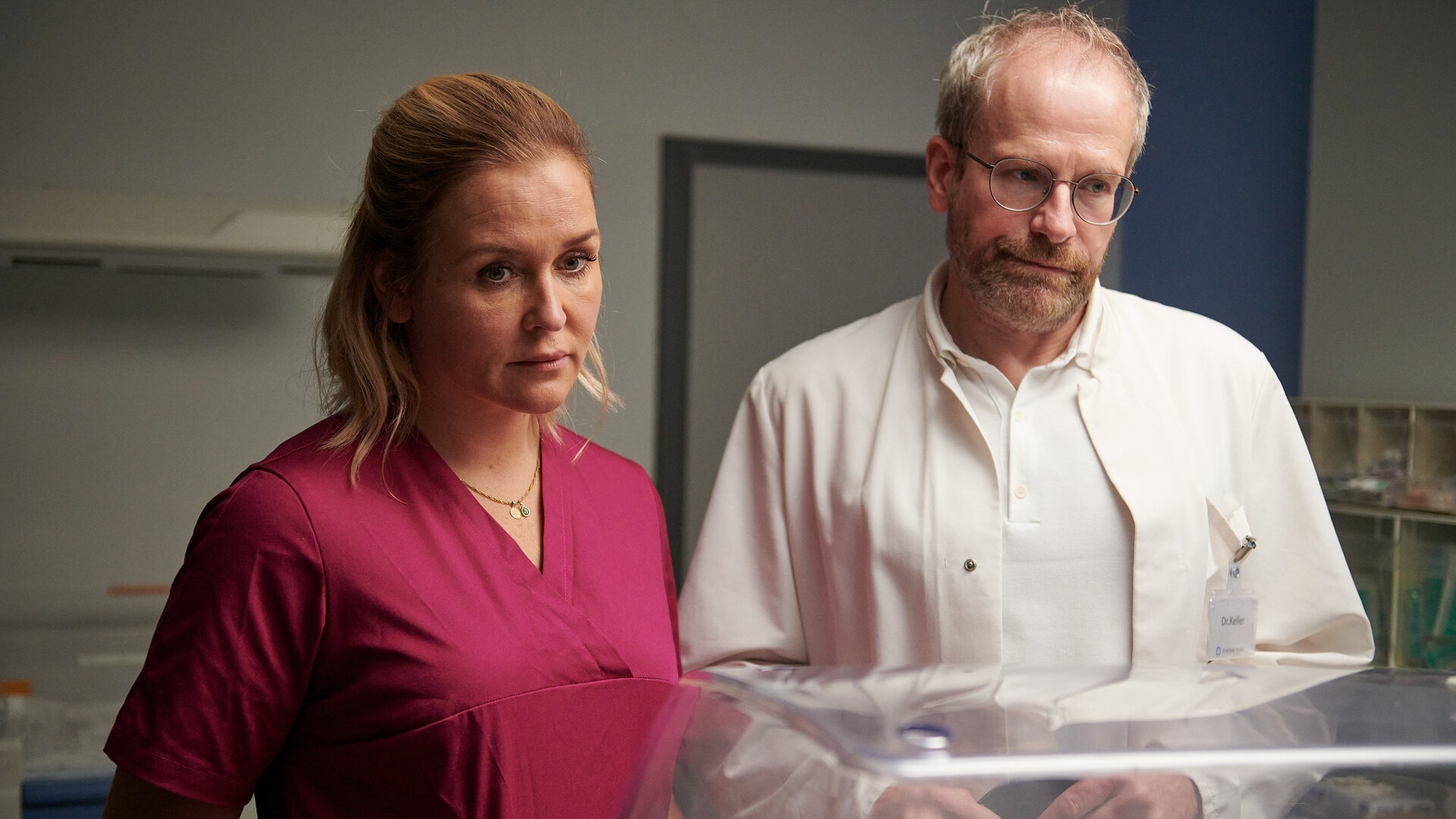 "Lena Lorenz - Fels in der Brandung: Im Intensivzimmer eines Krankenhauses stehen Lena Lorenz (Judith Hoersch) und Doktor Keller (Thomas Limpinsel) vor einem Brutkasten. Beide blicken ernst und wirken sehr betroffen.