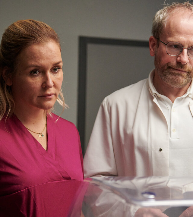 "Lena Lorenz - Fels in der Brandung: Im Intensivzimmer eines Krankenhauses stehen Lena Lorenz (Judith Hoersch) und Doktor Keller (Thomas Limpinsel) vor einem Brutkasten. Beide blicken ernst und wirken sehr betroffen.
