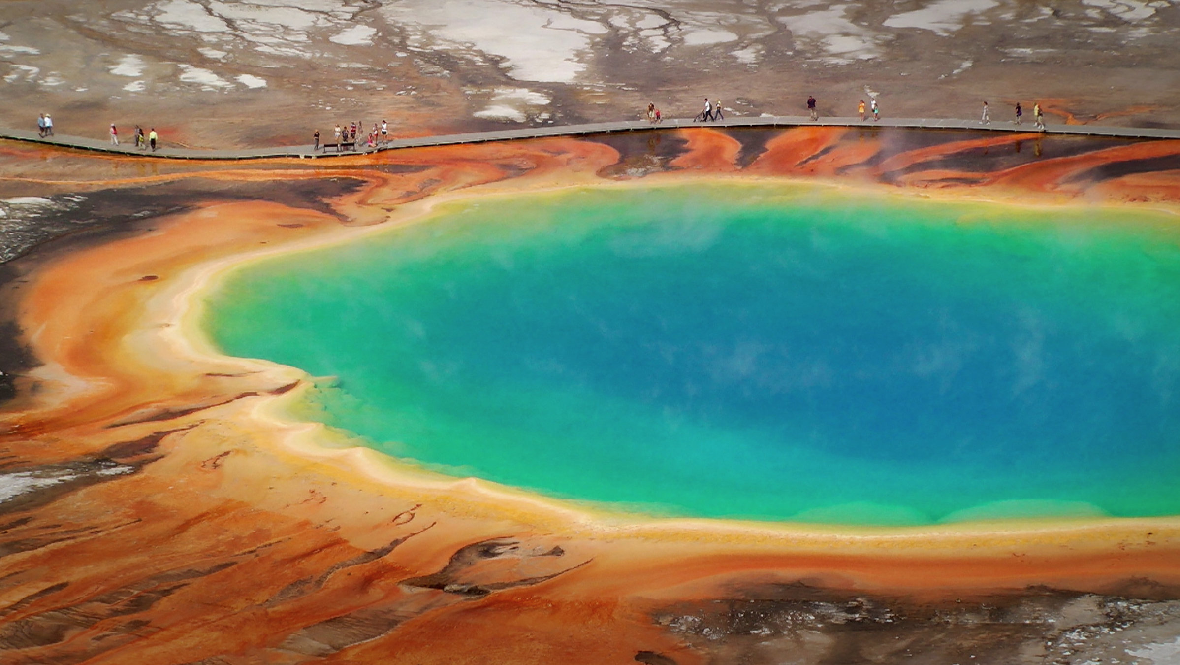 "Terra X: Die Macht der Vulkane - Im Schatten der Feuerberge": Aufnahme von einem türkisfarbenen See in einer Felswüsten-Landschaft. Auf einem Steg gehen Menschen am Rand des Sees entlang.