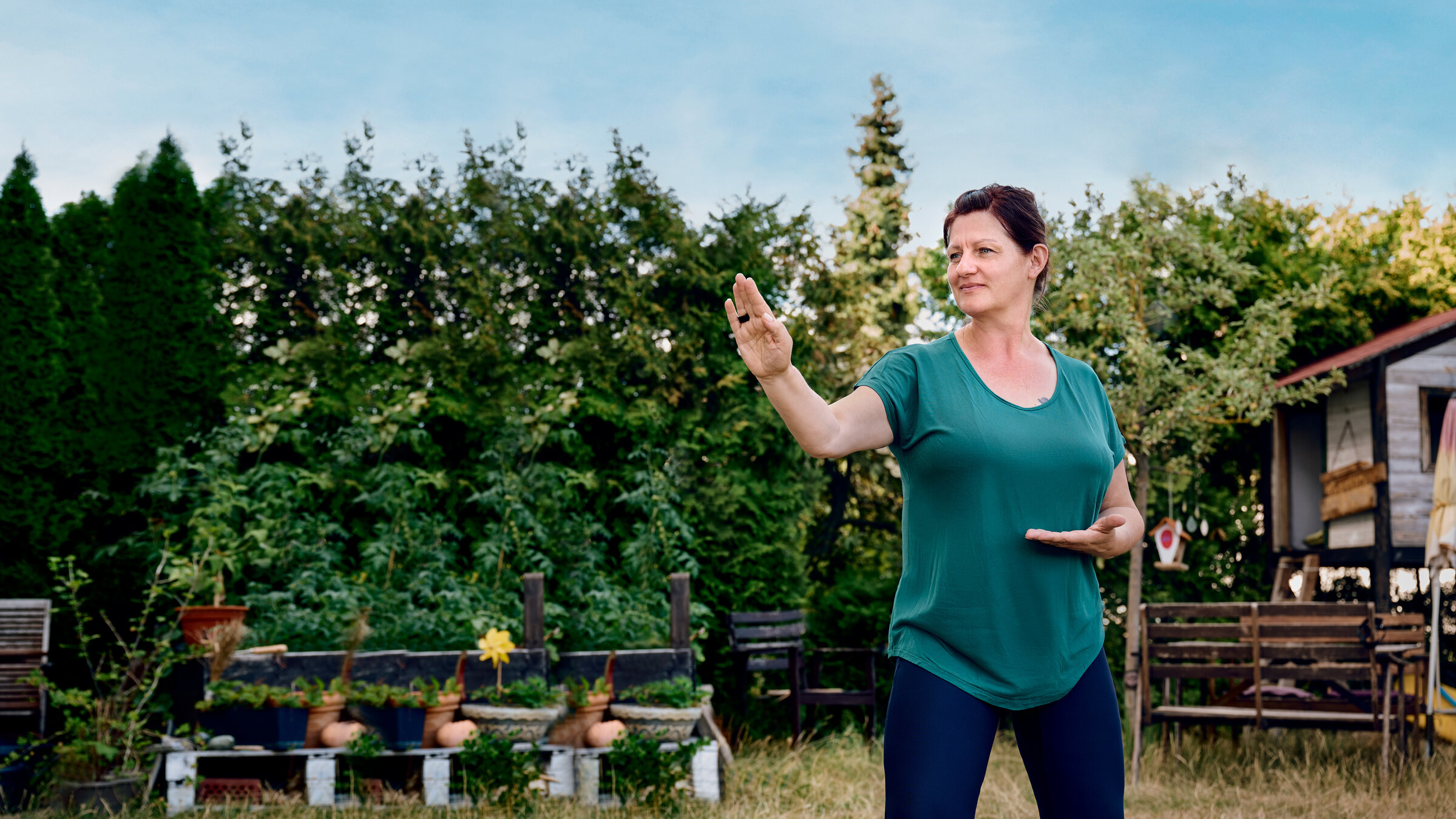 "einfach Mensch - Claudia: Mein Leben mit der Depression": Claudia steht im Garten und praktiziert Qi­gong.