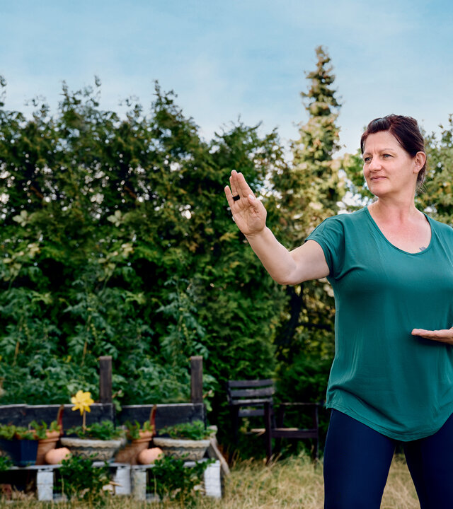 "einfach Mensch - Claudia: Mein Leben mit der Depression": Claudia steht im Garten und praktiziert Qi­gong.
