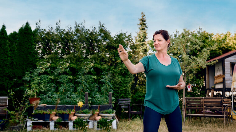 "einfach Mensch - Claudia: Mein Leben mit der Depression": Claudia steht im Garten und praktiziert Qi­gong.