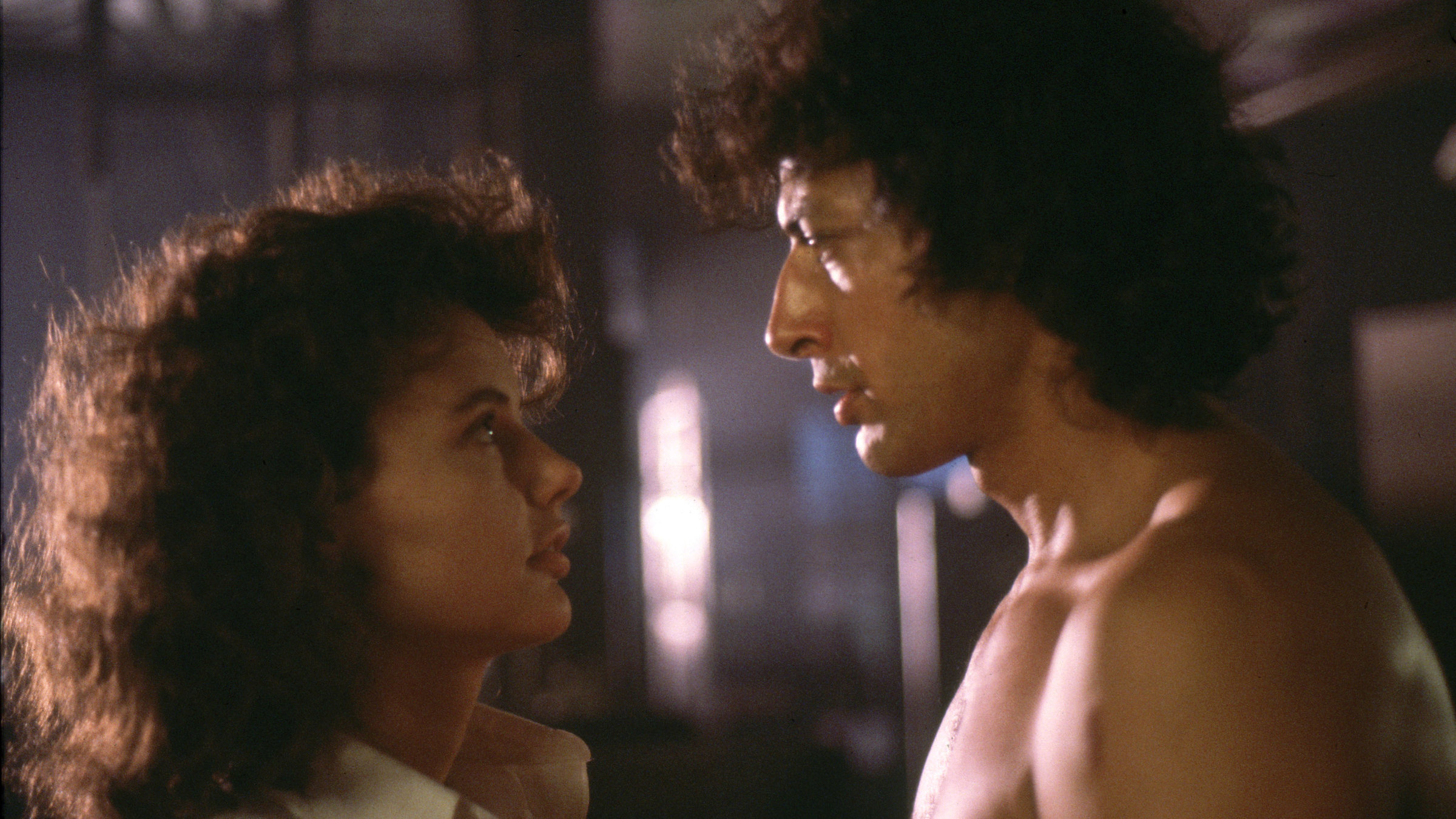 "Die Fliege": Seth Brundle (Jeff Goldblum) und Veronica Quaife (Geena Davis) stehen sich gegenüber und schauen sich innig an.