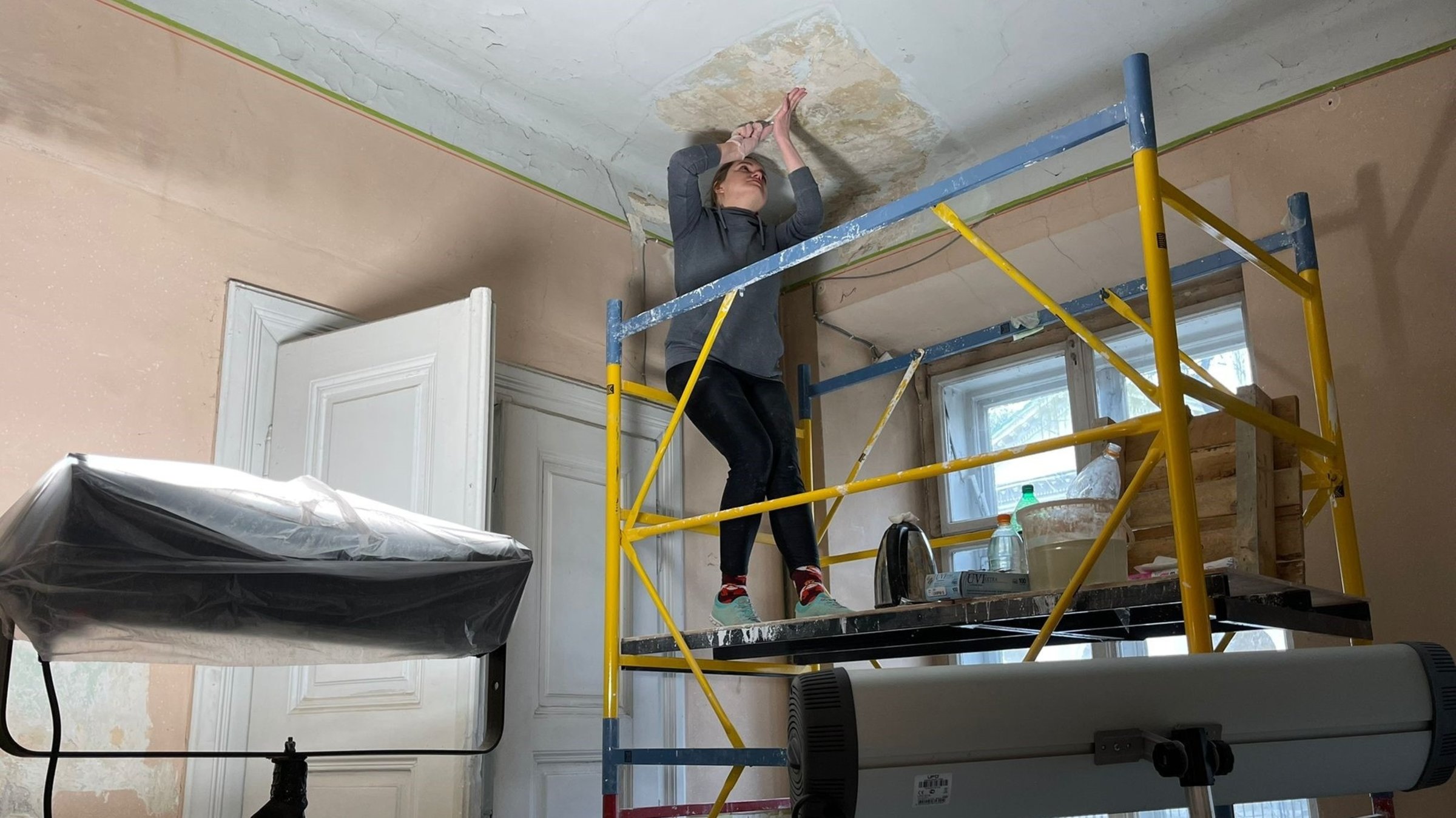 "Kunst im Krieg. Das neue Kulturleben in der Ukraine". Künstlerin steht auf Gerüst und restauriert einen Ausstellungsraum.