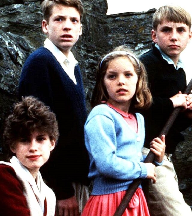 "Fünf Freunde auf Schmugglerjagd (2)": George (Jemima Rooper), Julian (Marco Williamson), Anne (Laura Petela) und Dick (Paul Child) stehen auf einer Steintreppe, umgeben von massiven Steinmauern, und blicken gespannt in die gleiche Richtung.
