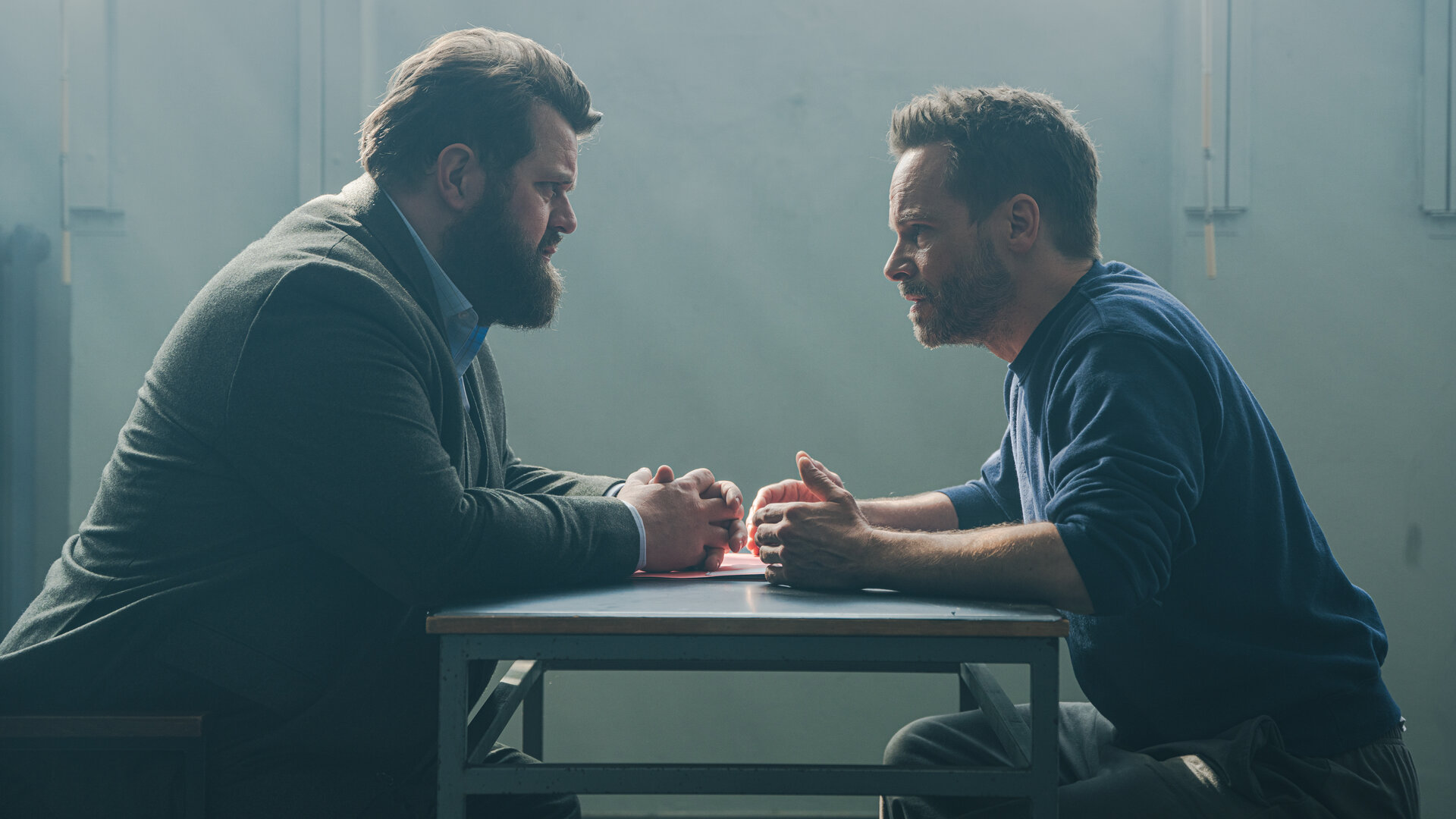 "Ein Fall für zwei - Falsches Spiel": In einem schlichten, kargen Verhörraum sitzen sich Benjamin Hornberg (Antoine Monot) und Leo Oswald (Wanja Mues) gegenüber. Im Hintergrund fällt Tageslicht durch ein vergittertes Fenster.
