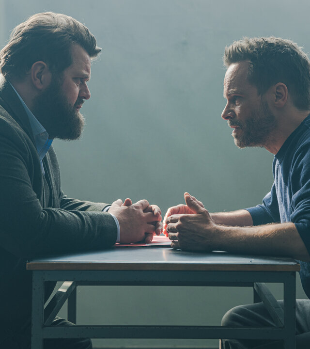 "Ein Fall für zwei - Falsches Spiel": In einem schlichten, kargen Verhörraum sitzen sich Benjamin Hornberg (Antoine Monot) und Leo Oswald (Wanja Mues) gegenüber. Im Hintergrund fällt Tageslicht durch ein vergittertes Fenster.