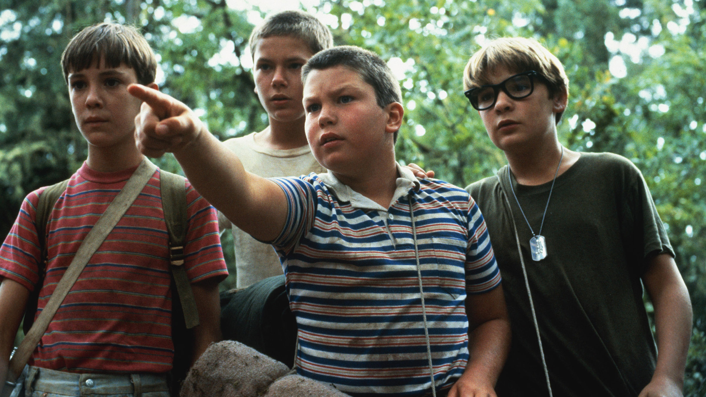 "Stand by Me - Das Geheimnis eines Sommers": Gordie (Wil Wheaton), Chris (River Phoenix), Teddy (Corey Feldman) und Vern (Jerry O´Connell) stehen nebeneinander im Wald und schauen aufmerksam in die Ferne, während Vern auf etwas zeigt.