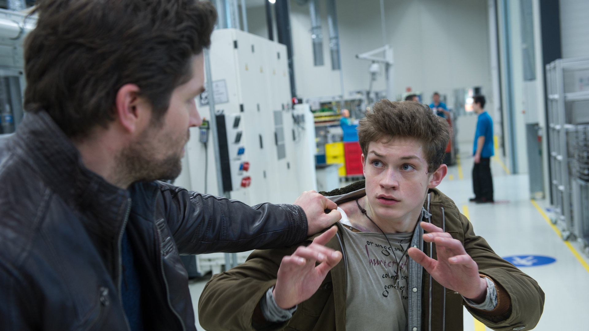 "SOKO Stuttgart - Kaiserbaby": Jo Stoll (Peter Ketnath) hat den jungen David Engstrom (Damian Hardung) am Anorak gepackt. Beide befinden sich in einer Werkshalle. Im Hintergrund sind Werksarbeiter zu sehen.