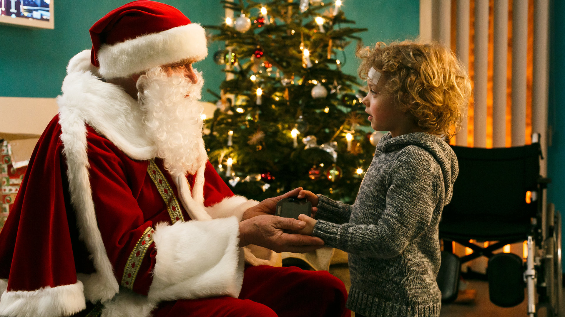 "Bettys Diagnose - Schöne Bescherung": Der Weihnachtsmann (Jürgen Heinrich) übergibt dem kleinen Felix (Otto Koch) ein Geschenk. Im Hintergrund ist ein geschmückter Weihnachtsbaum zu sehen.