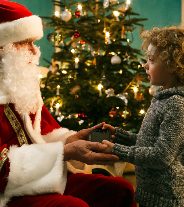 "Bettys Diagnose - Schöne Bescherung": Der Weihnachtsmann (Jürgen Heinrich) übergibt dem kleinen Felix (Otto Koch) ein Geschenk. Im Hintergrund ist ein geschmückter Weihnachtsbaum zu sehen.