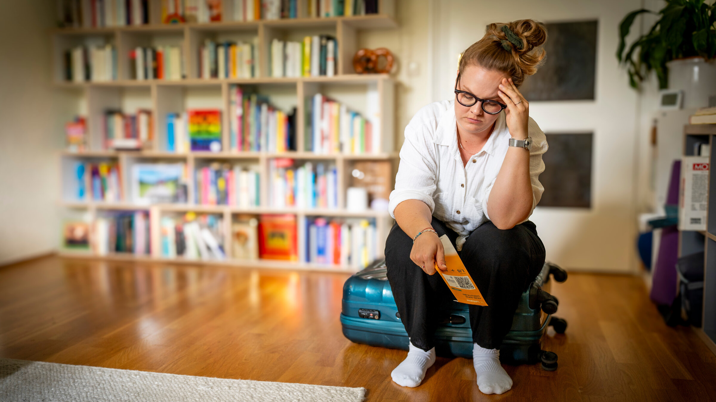 "37°Leben: Wenn die Panik mitfliegt - Flugangst besiegen": Sophie (33) sitzt auf einem Koffer in ihrem Wohnzimmer und hat ein Flugticket in der Hand. Ihr Kopf ist mit einer Hand aufgestützt und ihr Gesichtsausdruck zeigt ihre Sorge und Angst.