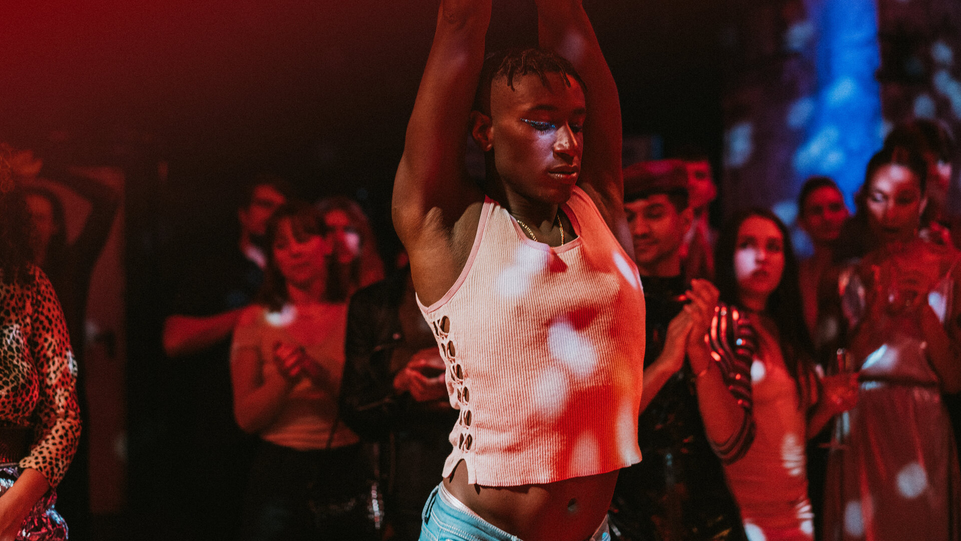 "House of Bellevue - New Way": Emm (Ricco-Jarret Boateng) tanzt mit geschlossenen Augen, seine Arme sind nach oben gestreckt. Im Hintergrund stehen zahlreiche Personen (Komparsen), die klatschen.