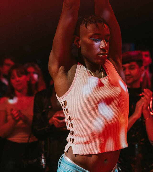 "House of Bellevue - New Way": Emm (Ricco-Jarret Boateng) tanzt mit geschlossenen Augen, seine Arme sind nach oben gestreckt. Im Hintergrund stehen zahlreiche Personen (Komparsen), die klatschen.