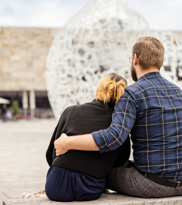"37°Leben: Arm an der Uni - Wenn das Studium alles kostet": Selina und Dennis sitzen mit dem Rücken zur Kamera auf einer Bank auf einem Platz.  Sie sitzen Arm in Arm nebeneinander.