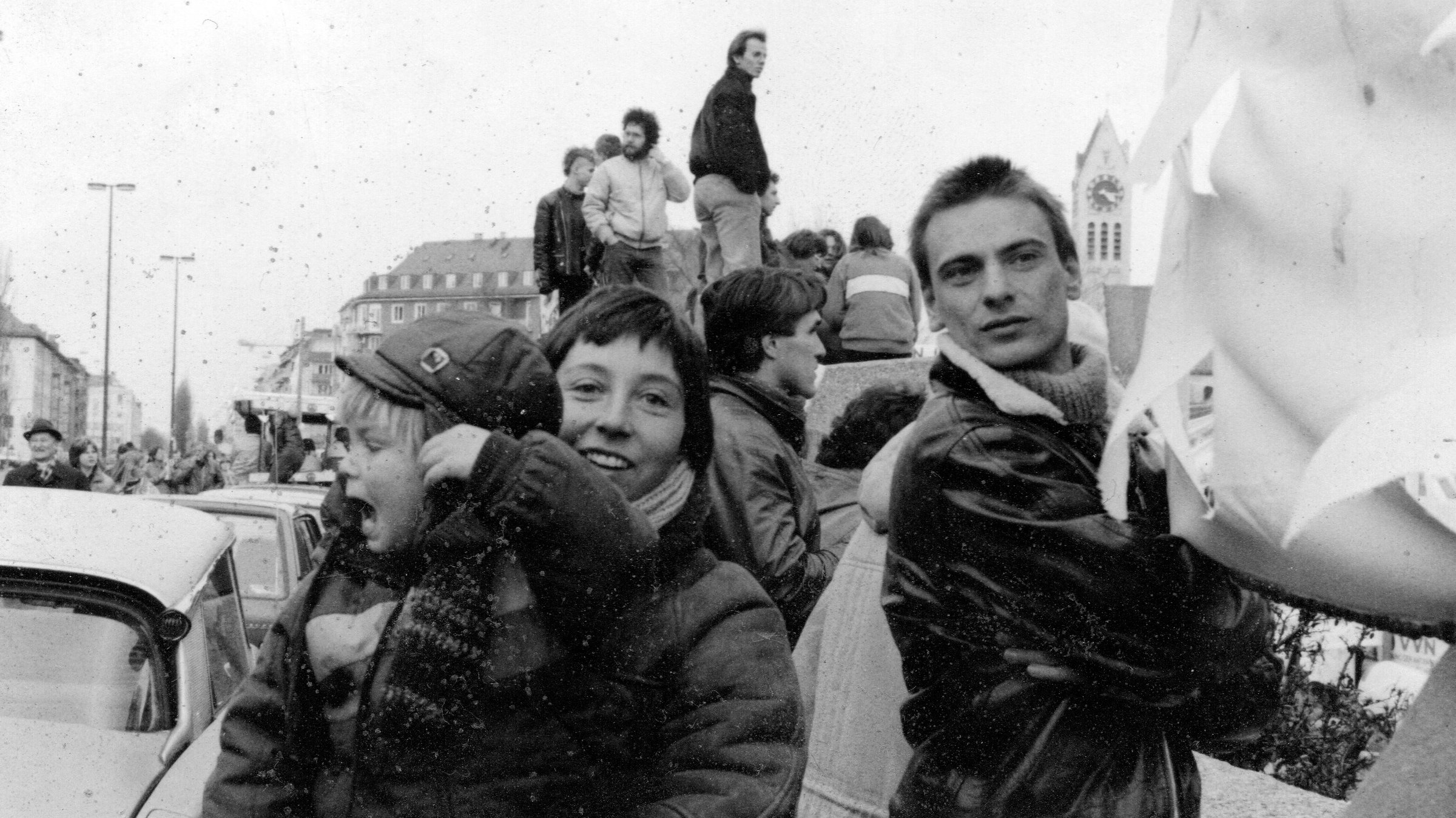 "Mein Opa, Karin und ich": Auf einer Schwarz-Weiß-Aufnahme sind Teilnehmer, teilweise auf einer Mauer stehend, während einer Demonstration zu sehen. Im Vordergrund hält Karin Springer ihren Sohn Moritz im Arm und lächelt in die Kamera. Ihr Mann Bernhard Springer steht neben ihr.