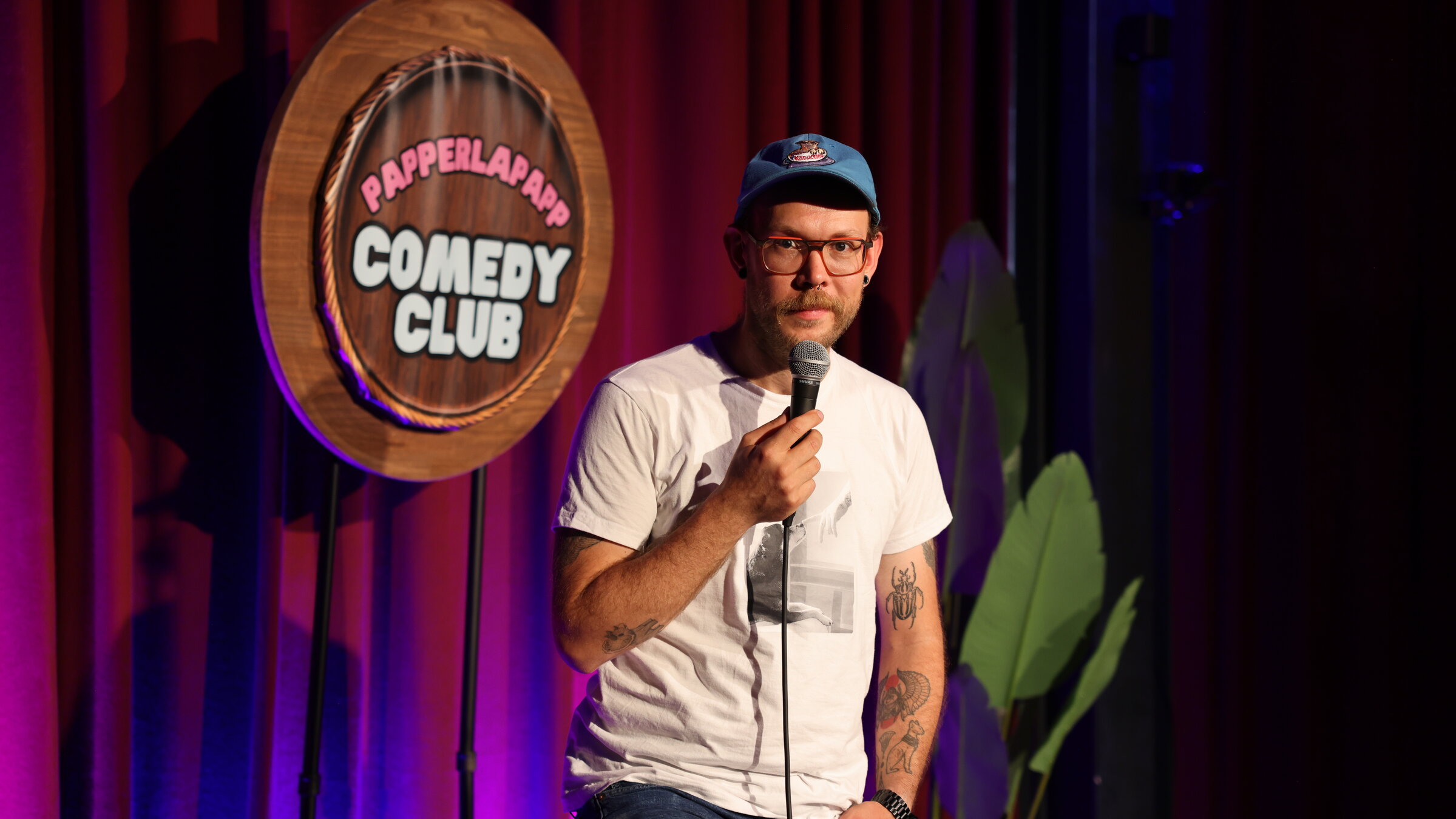 "Einfach Mensch - Lacht ruhig über mich!": Toby Käp steht auf einer Bühne mit einem Mikrofon in der Hand.