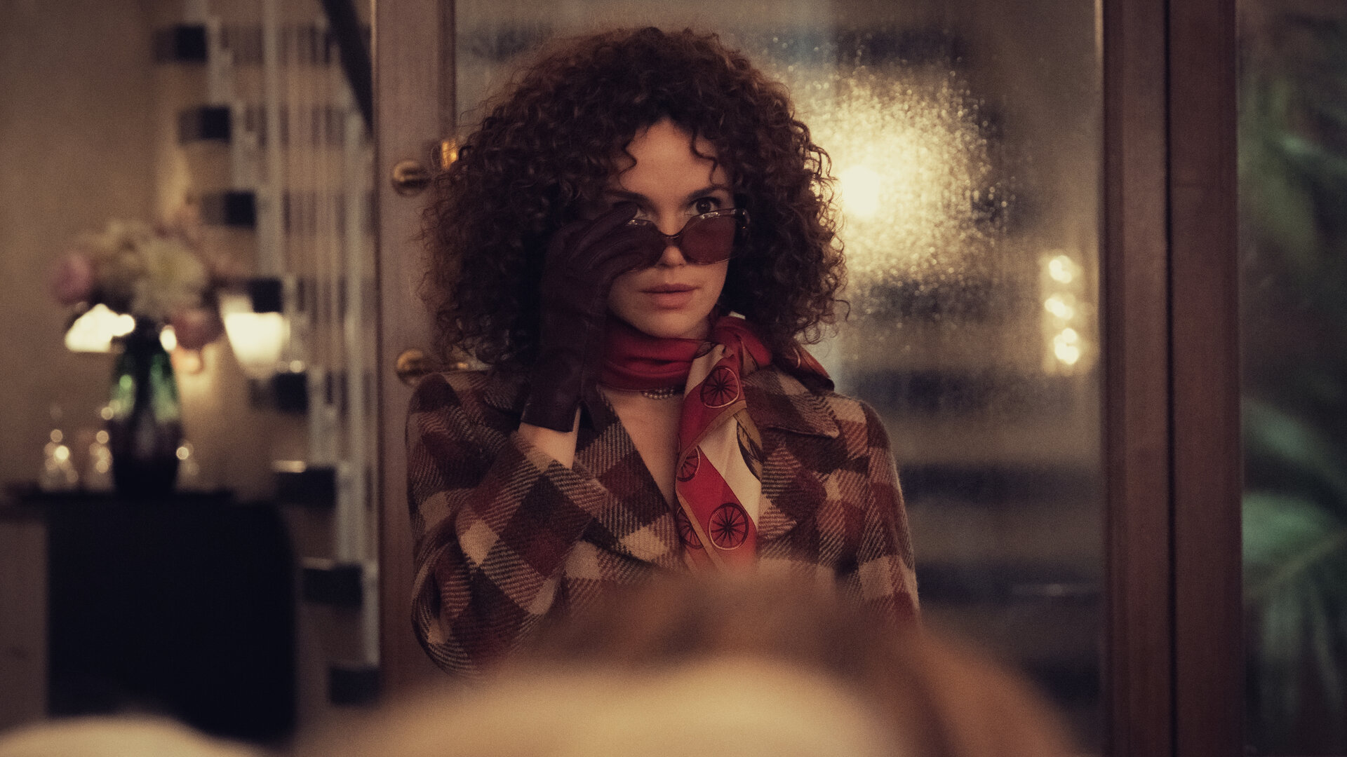 "Ku'damm 77": Im Türrahmen des Saals steht Eva Fassbender (Emilia Schüle). Sie trägt eine Sonnenbrille und zieht diese leicht von den Augen.