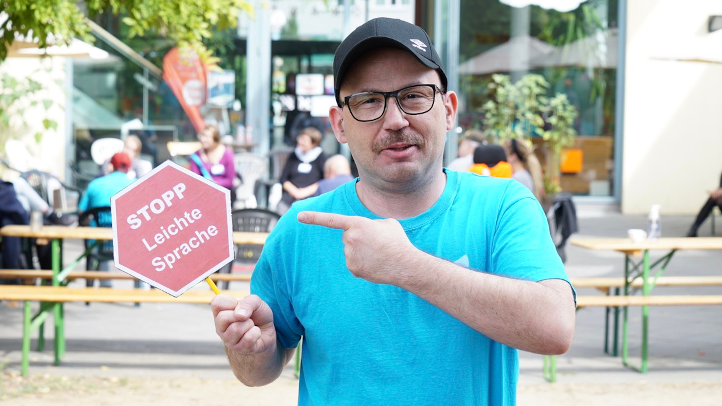Sascha Ubrig hält ein Schild hoch auf dem „Stopp Leichte Sprache“ steht. Eine Forderung von Menschen mit Behinderung, Texte so verständlich wie möglich zu gestalten.