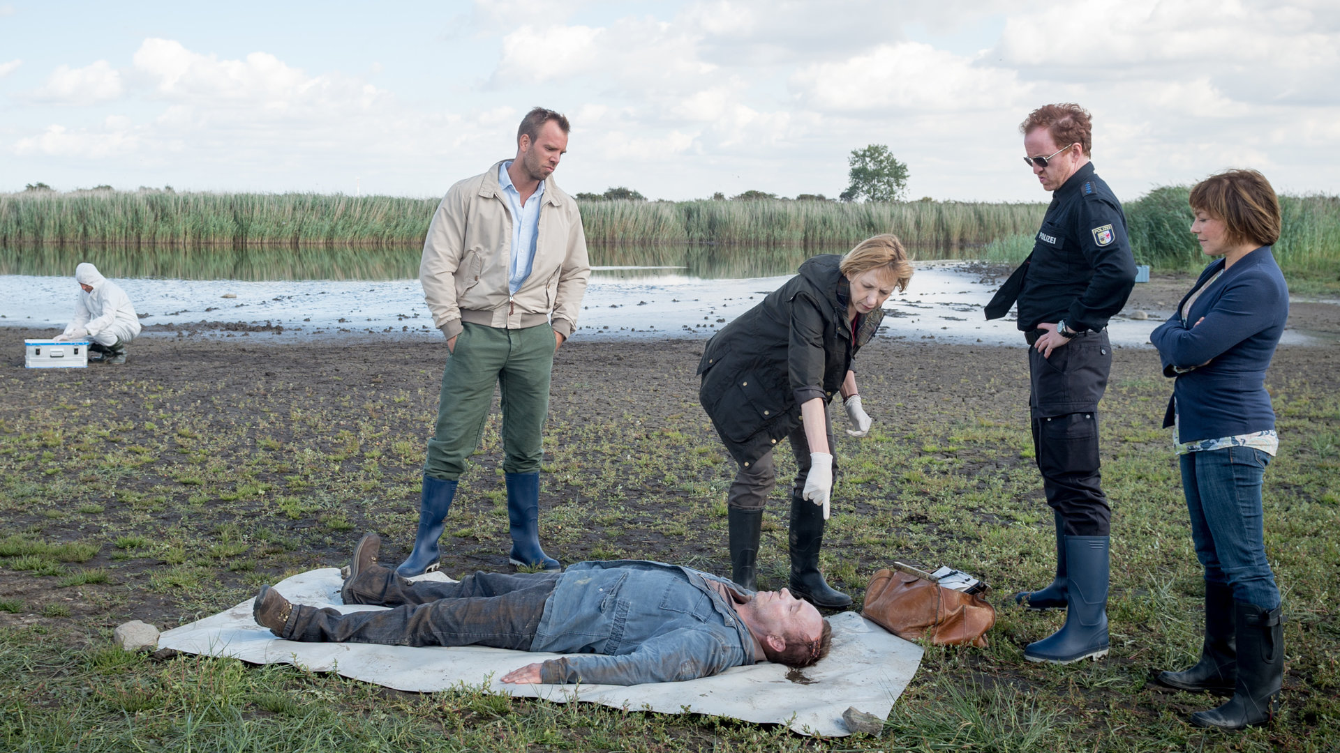 "SOKO Wismar – Rote Erna“: Lars Pöhlmann (Dominic Boeer), Helene Sturbeck (Katharina Blaschke), Kai Timmermann (Matthias Junge) und Katrin Börensen (Claudia Schmutzler) inspizieren die Leiche von Paul Gödecke (Thomas Sobotzki), die auf einer Plane im Feld liegt.