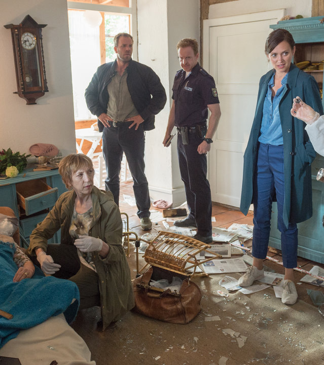 „SOKO Wismar – Blindgänger“: KT-Expertin Roswitha Prinzler (Silke Matthias) zeigt den Kollegen Pöhlmann (Dominic Boeer), Karoline Joost (Nike Fuhrmann) und Timmermann (Mathias Junge) die hochgegangene Gewehrgranate. Dr. Helene Sturbeck (Katharina Blaschke) kniet neben er Leiche von Barbara Voss (Ulrike Lodwig), die auf einem Sofa in ihrem völlig verwüsteten Wohnzimmer liegt.
