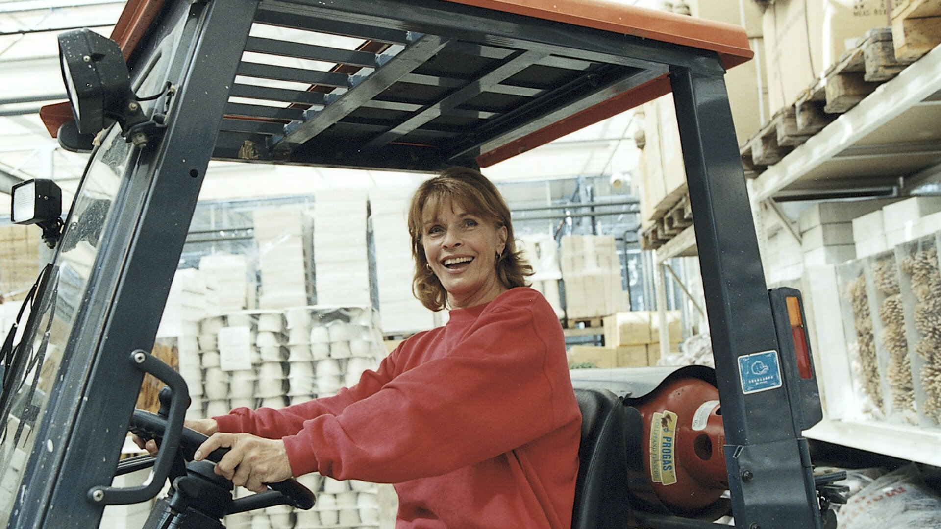 "Die schnelle Gerdi und die Hauptstadt – Die München-Connection": Gerdi (Senta Berger) sitzt lachend am Steuer eines Gabelstaplers in einem Dekogeschäft.