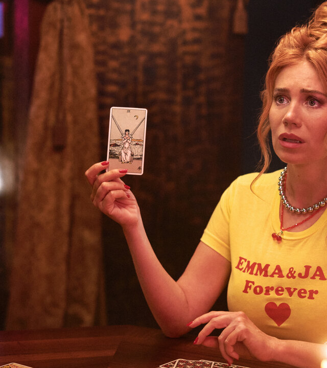 "My Ex - Paul": Ivy (Palina Rojinski) sitzt in einem dunklen Raum am Tisch und hat aus all den Karten, die auf dem Tisch liegen, eine herausgezogen. Sie hält sie mit ihrer rechten Hand nach oben. Auf dem Tisch stehen brennende Kerzen, im Hintergrund spendet eine Wandleuchte spärliches Licht.