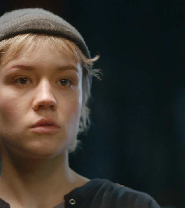 "Becoming Charlie - Mehr als Entweder Oder": Porträt von Charlie (Lea Drinda). Sie trägt eine dunkle Strickmütze und steht vor dunklem Hintergrund.