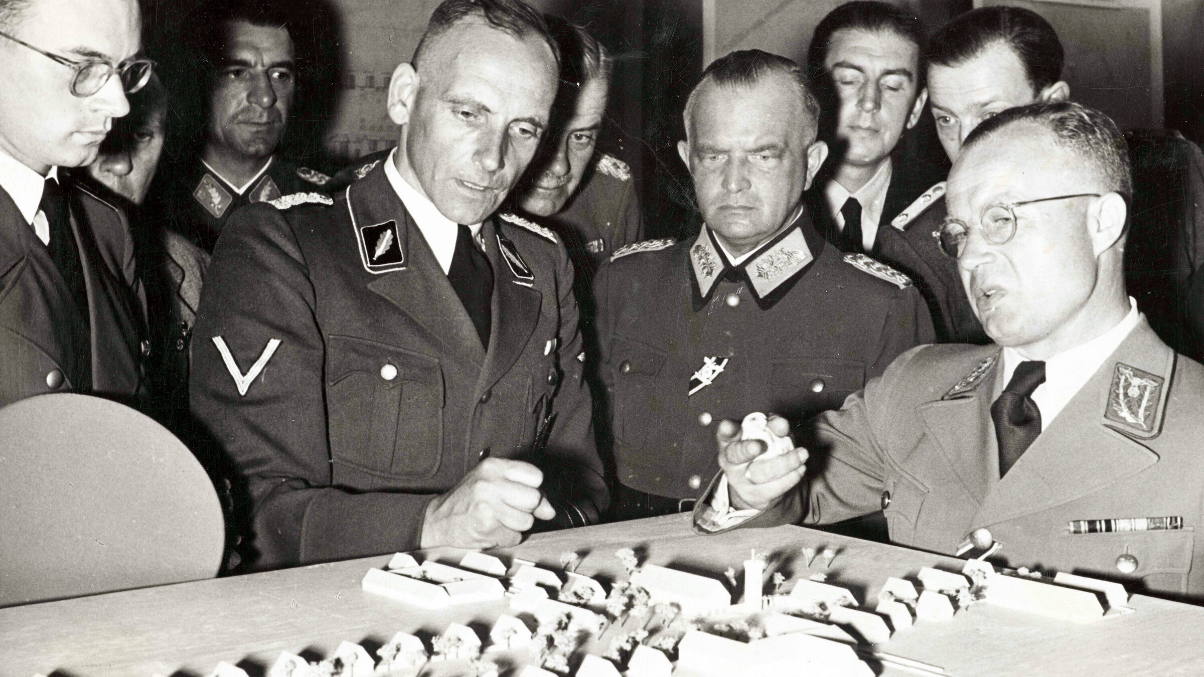 "Blutiger Boden, deutscher Raum – Die Siedlungspläne der SS": Prof. Dr. Konrad Meyer (4. v.l.) vor einem Dorfmodell der Ausstellung „Planung und Aufbau im Osten“ (1941).