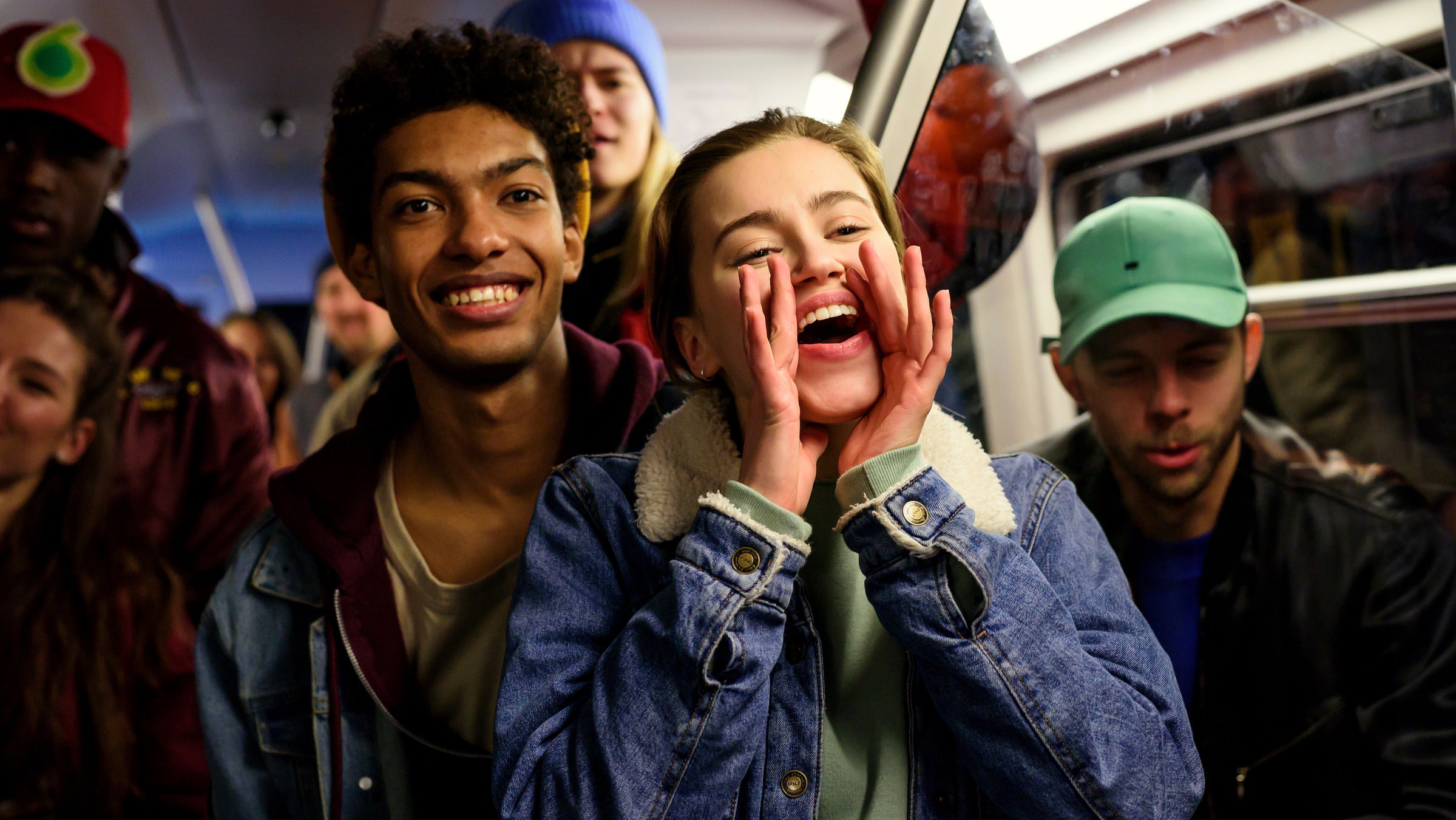 "Into the Beat – Dein Herz tanzt": Ein dichtgedrängtes Gruppenbild in einem U-Bahn-Wagen: Katya (Alexandra Pfeifer) hat die Hände zu einem Trichter um den Mund gelegt und feuert begeistert jemanden an. Hinter ihr steht Marlon (Yalany Marschner) und andere junge Menschen. Sie alle beobachten lachend das, was ihnen offenbar gerade vorgeführt wird.