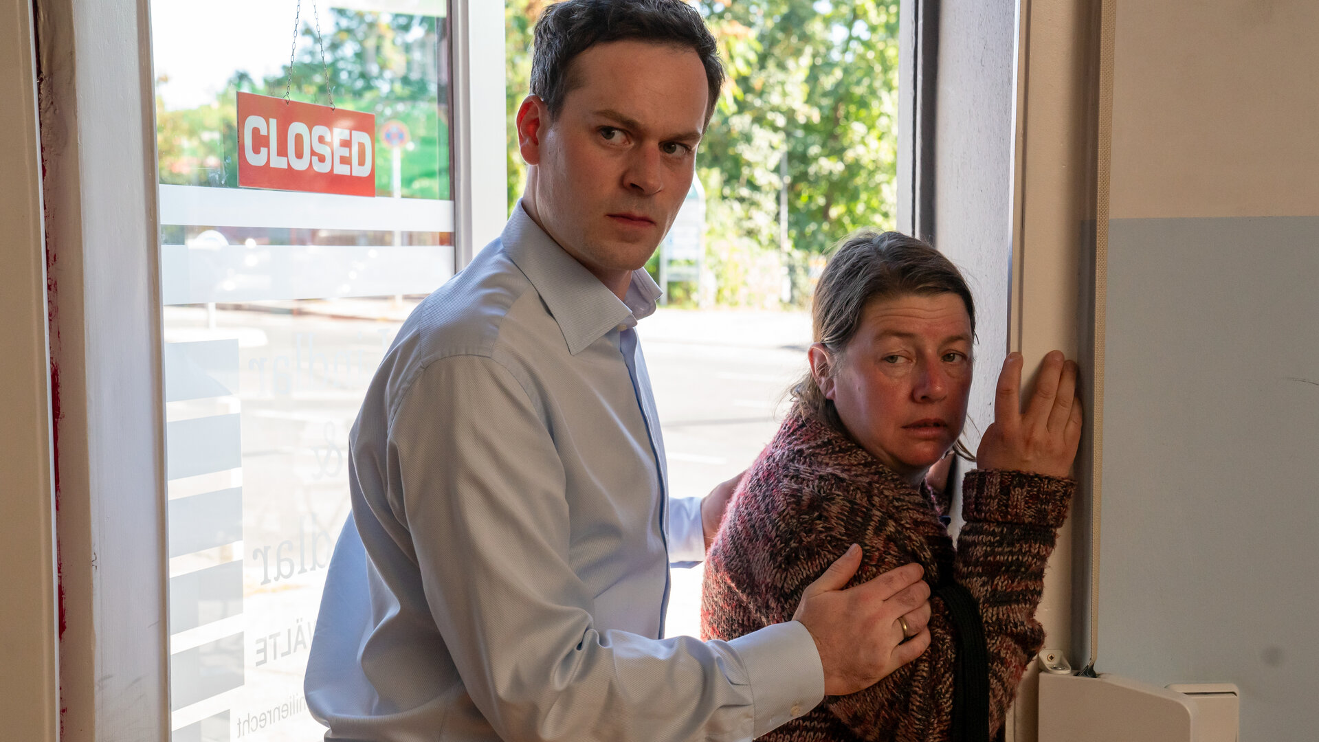 "Letzte Spur Berlin - Rückfall": Anwalt Konstantin Lindlar (Florian Bartholomäi) hält mit beiden Armen die unliebsame Besucherin Petra Fischer (Tilla Kratochwil) an einer Eingangstür von hinten fest. Petra Fischer versucht sich am Türrahmen festzuhalten.