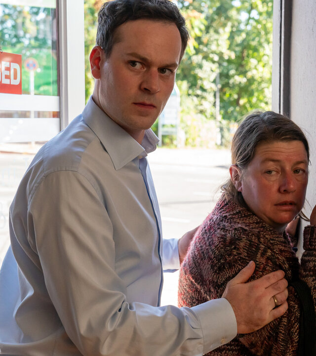 "Letzte Spur Berlin - Rückfall": Anwalt Konstantin Lindlar (Florian Bartholomäi) hält mit beiden Armen die unliebsame Besucherin Petra Fischer (Tilla Kratochwil) an einer Eingangstür von hinten fest. Petra Fischer versucht sich am Türrahmen festzuhalten.