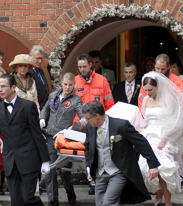"Die Rettungsflieger - Für immer und ewig": Das Team der Rettungsflieger trägt bei einer Hochzeit eine Person aus der Kirche. Drum herum stehen die Hochzeitsgäste und die Braut Patricia Falkenstein (Anna Bertheau) läuft mit gerafften Röcken neben der Trage her.