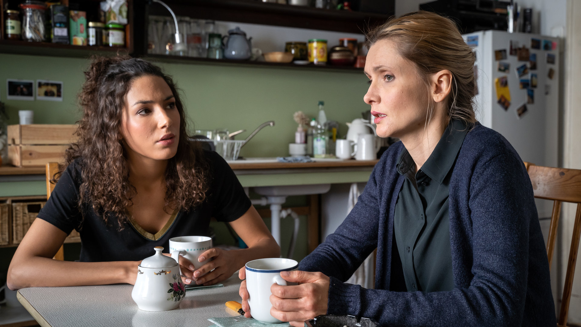 "SOKO Leipzig - Dem Tode geweiht": Kim Nowak (Amy Mußul) sitzt neben Katrin Graber (Alexandra Finder) am Küchentisch in der Küche von Katrin. Beide halten eine Tasse in den Händen. Kim hört Katrin aufmerksam zu.
