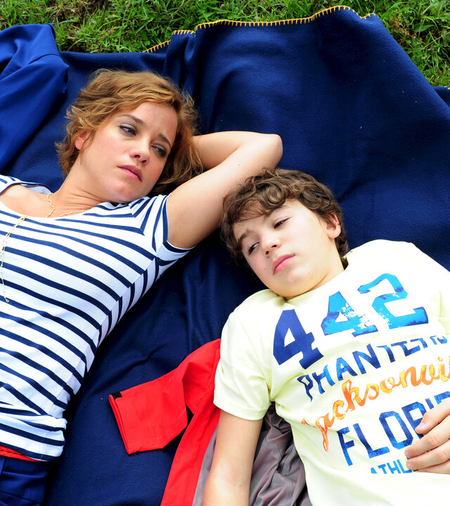 "Ein Sommer in den Bergen": Blick von oben: Müde liegen Pia Vandenbrok (Muriel Baumeister) und ihr Sohn Leo (Jannis Michel) nebeneinander auf dem Rücken im Gras.