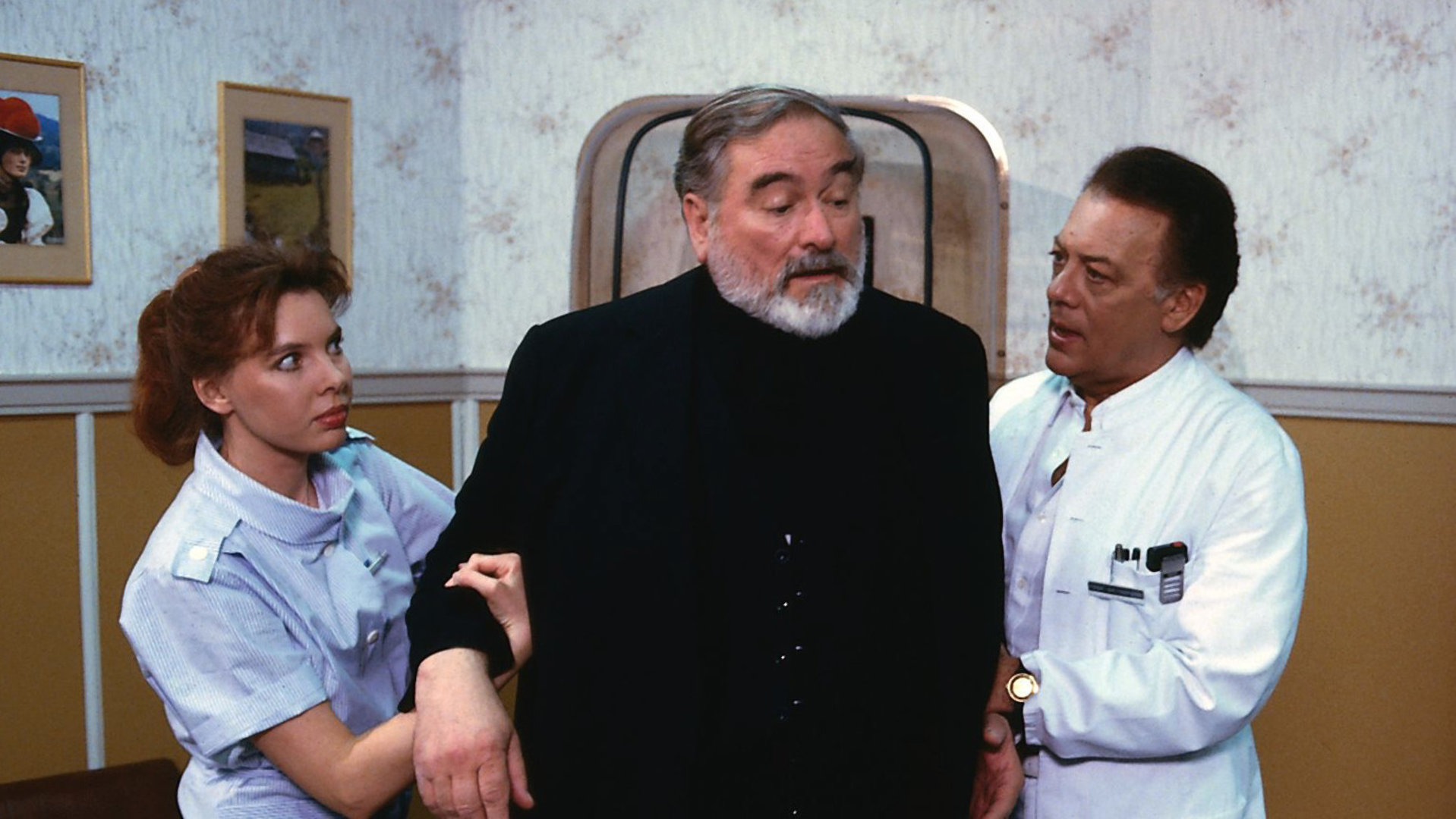 "Die Schwarzwaldklinik - Wie du mir, so ich dir": Pfarrer Kleinschmidt (Hans Wyprächtiger) wird von Prof. Brinkmann (Klausjürgen Wussow) und Schwester Ina (Gaby Fischer) gestützt.