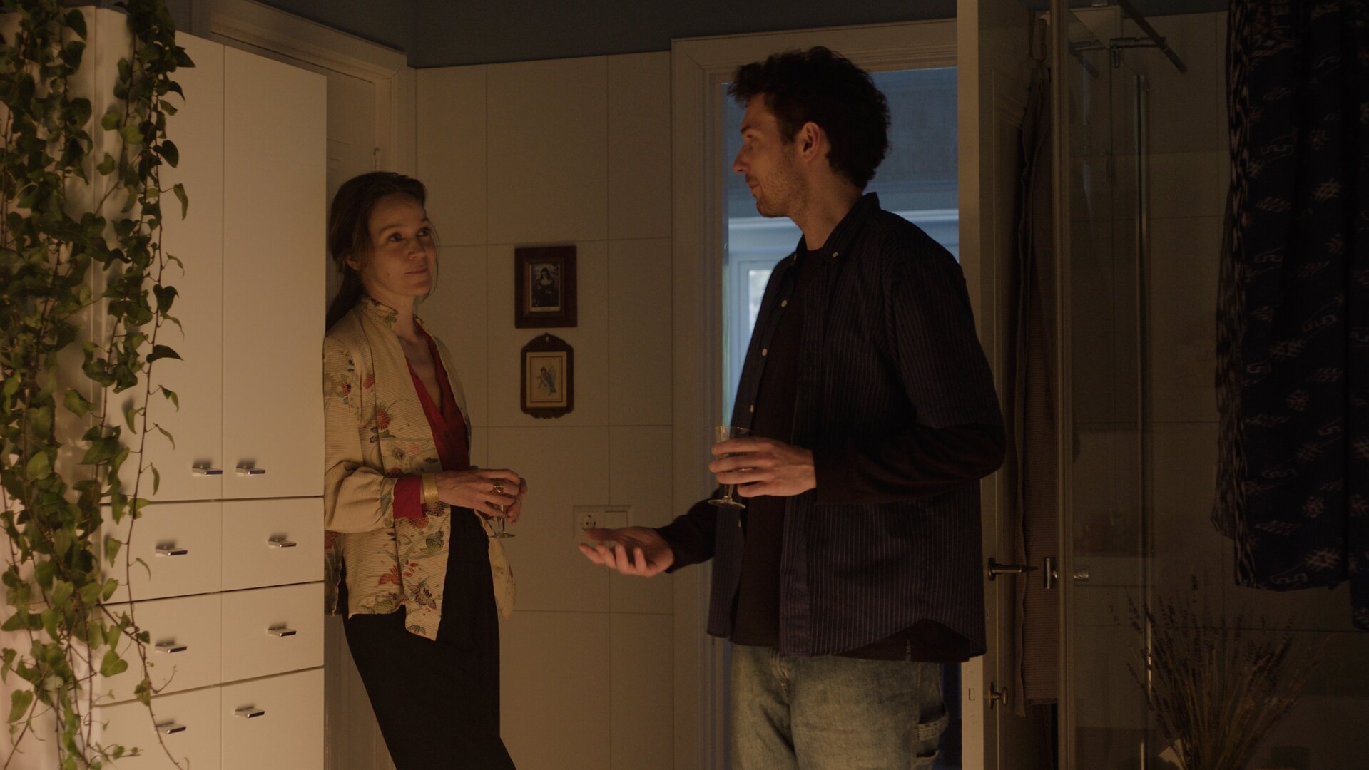 "This Is Gonna Be Great - Familie": David (Rein Mulder) steht in einem Raum vor einer geöffneten Tür. Neben ihm lehnt Monika (Jeanette Hain) an einem Schrank. Die beiden sprechen miteinander.