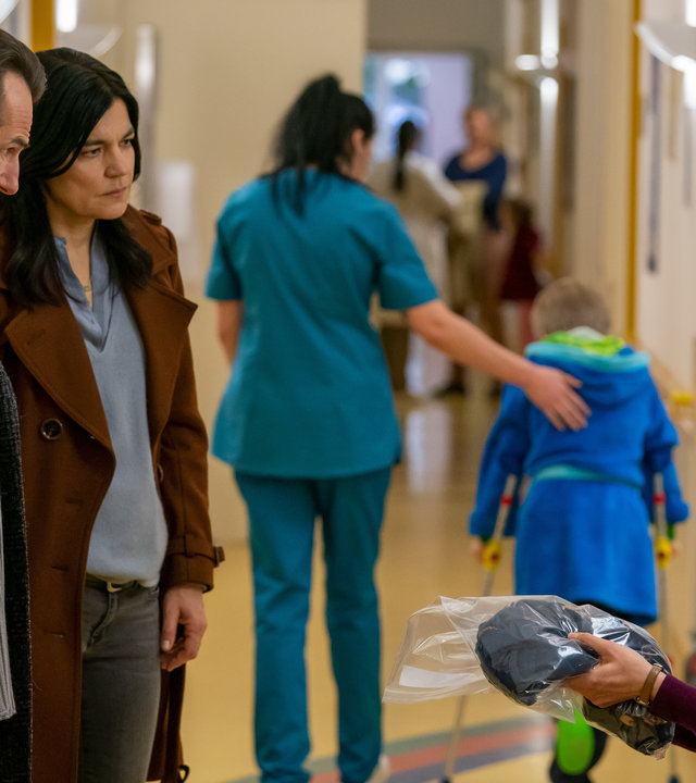 "Letzte Spur Berlin - Sorgenkind": Radek (Hans-Werner Meyer) und Mina (Jasmin Tabatabai) stehen in einem Krankenhausflur. Ihnen gegenüber sitzt Janina (Katrin Röver), die den Schlafanzug ihres Sohnes entgegennimmt. Sie schaut sehr besorgt zu Radek und Mina auf.