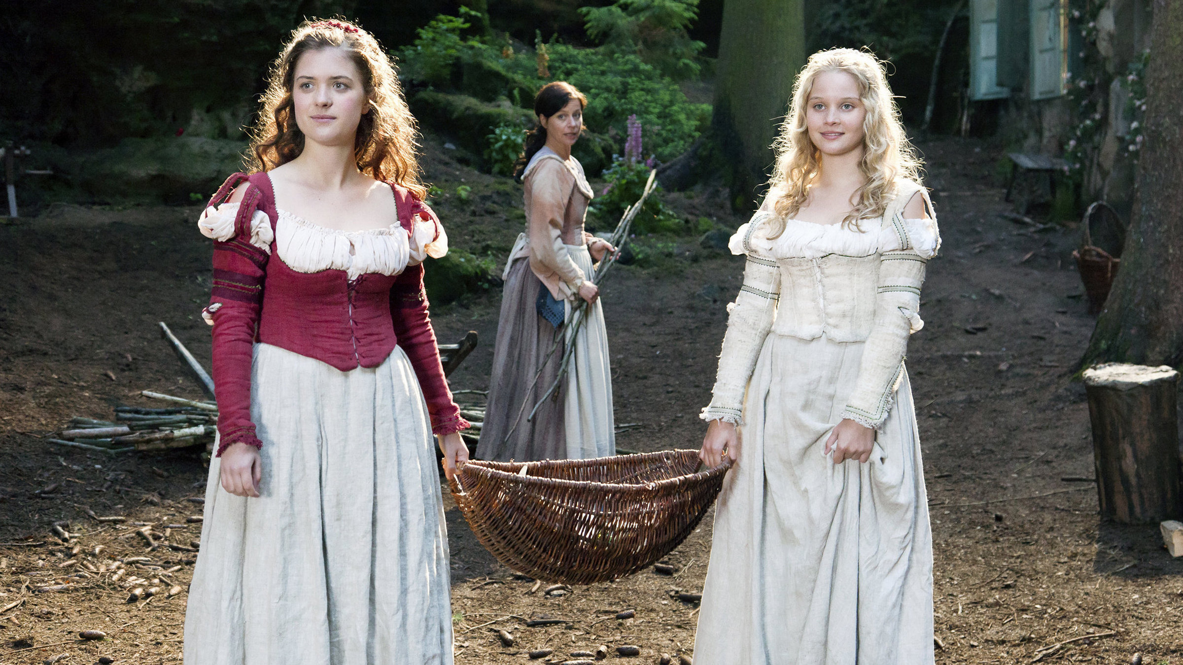 "Schneeweißchen und Rosenrot": Schneeweißchen (Sonja Gerhardt, rechts) und Rosenrot (Liv Lisa Fries, links) brechen mit einem Korb voll Rosenölfläschchen zum Markt auf.  Ihre Mutter (Jule Ronstedt, mitte) ist in Sorge, ihre Töchter allein in die Stadt gehen zu lassen.