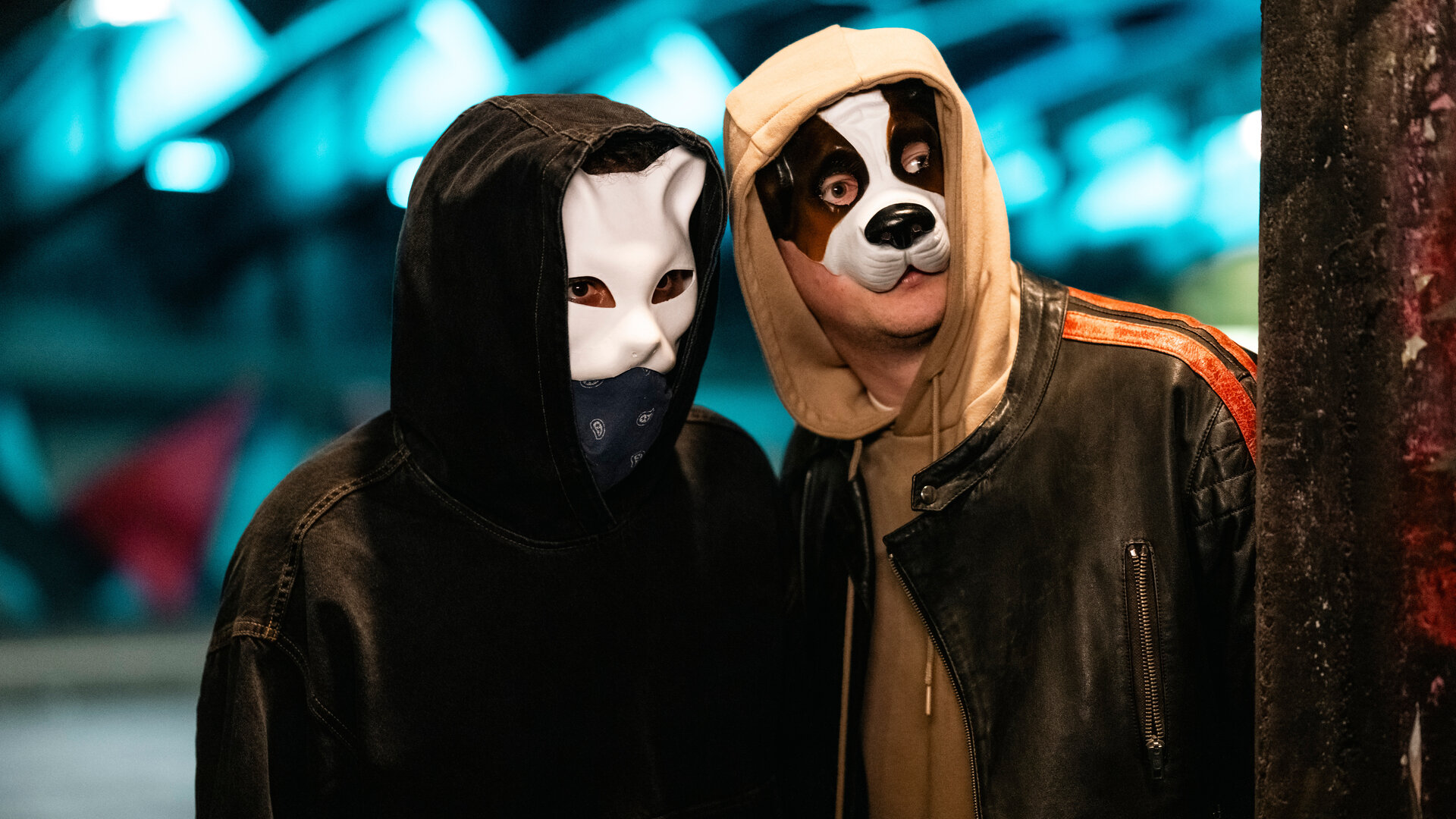 "SOKO Köln - Der tote Hund": Robert Kapp (Nils Kretschmer) hat sich die Kapuze seines Hoodies ins Gesicht gezogen und trägt eine Hundemaske. Er steht dicht neben einer unbekannten Person, die ebenfalls die Kapuze auf dem Kopf und eine Tiermaske über dem Gesicht trägt. Beide blicken angespannt zur Seite.
