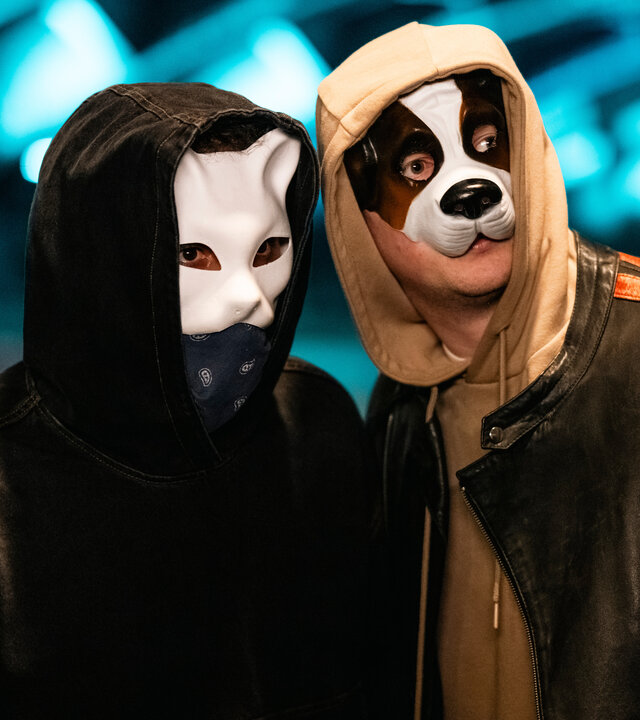 "SOKO Köln - Der tote Hund": Robert Kapp (Nils Kretschmer) hat sich die Kapuze seines Hoodies ins Gesicht gezogen und trägt eine Hundemaske. Er steht dicht neben einer unbekannten Person, die ebenfalls die Kapuze auf dem Kopf und eine Tiermaske über dem Gesicht trägt. Beide blicken angespannt zur Seite.