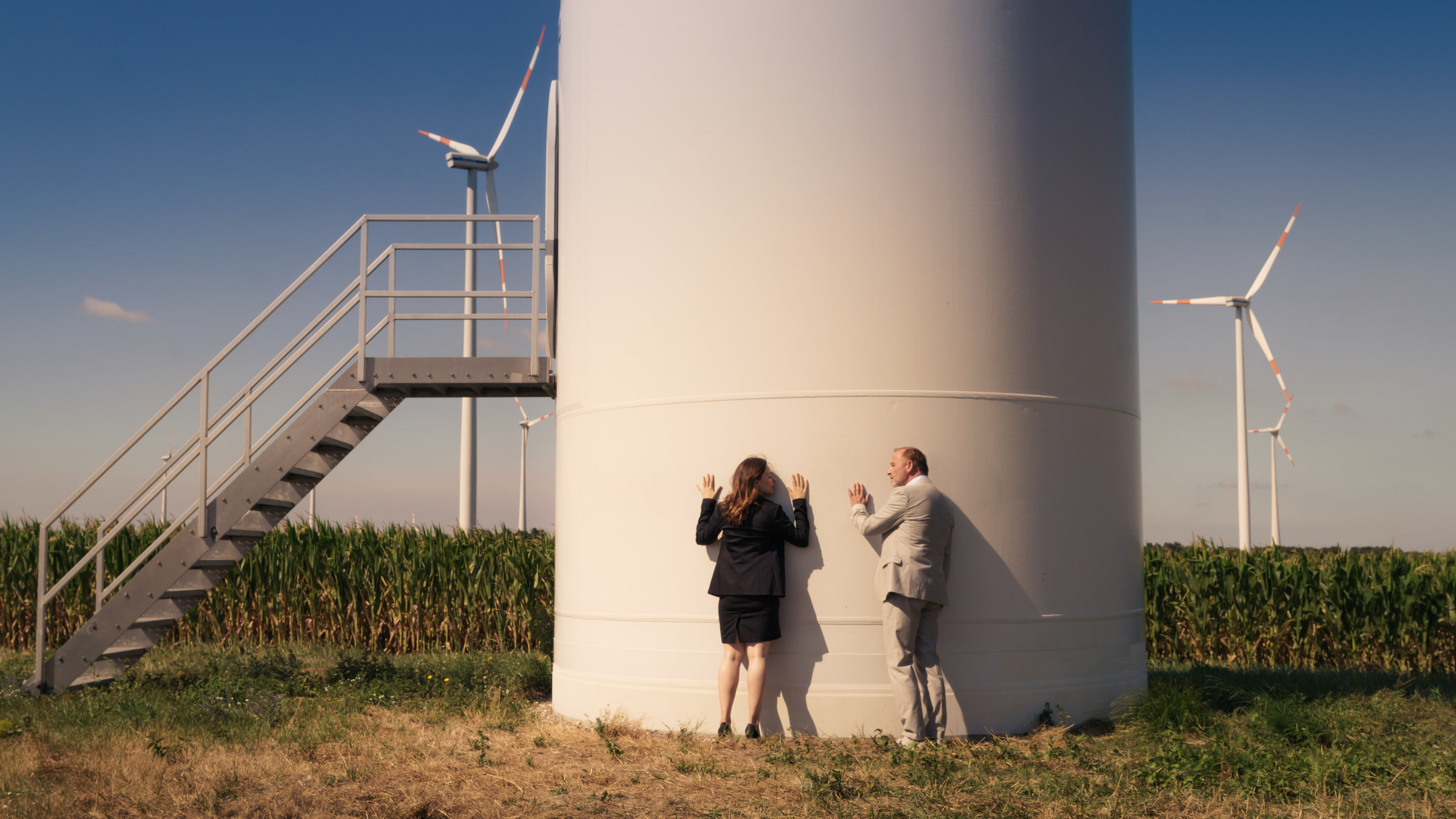 "Unterleuten - Das zerrissene Dorf (2)": Unternehmer Konrad Meiler (Alexander Held) und Frau Pilz (Mina Tander) stehen am Sockel eines Windrades. Beide halten die Hände an den Beton.